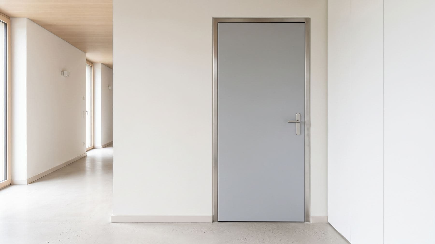 Bloc-porte blindé gris clair fermé dans une entrée contemporaine, huisserie inox et poignée minimaliste