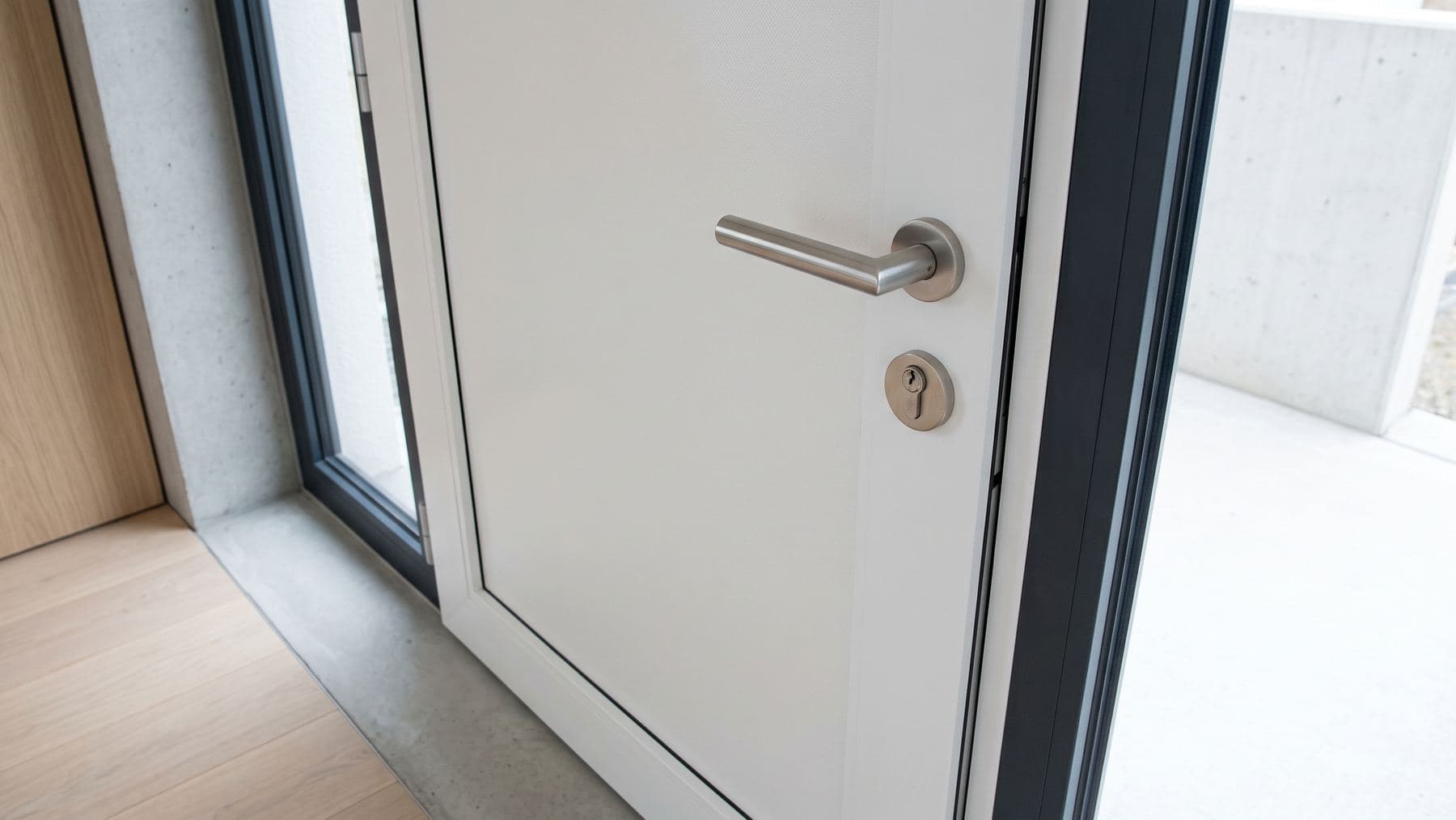 Porte d’entrée en PVC blanc légèrement désaffleurée dans son dormant, jeu irrégulier visible au niveau du pêne