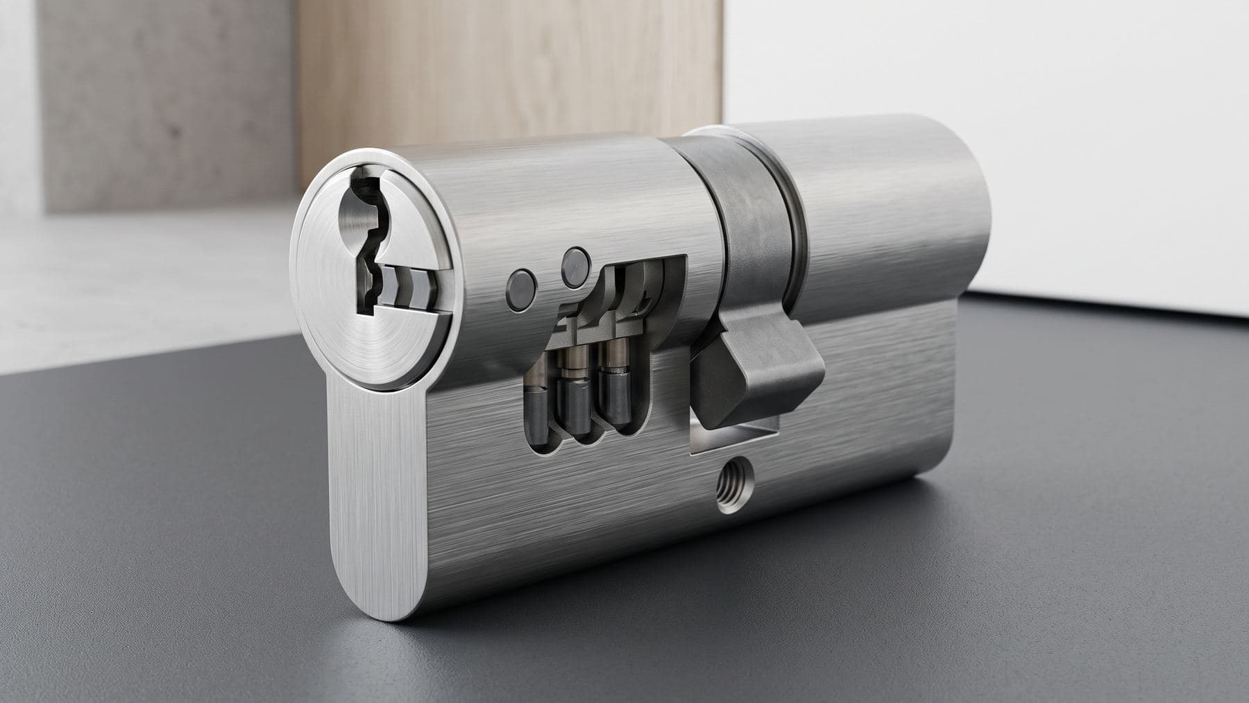 Macro d’un cylindre haute sécurité en acier brossé, inserts anti-perçage et came renforcée visibles, sur un plan gris foncé
